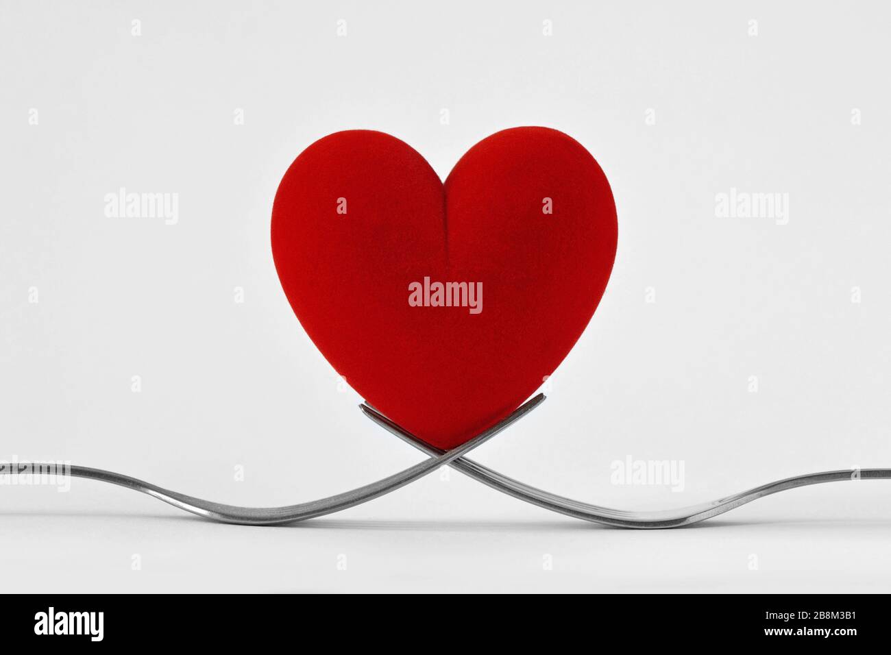 Due forcelle che tengono un cuore su sfondo bianco - concetto di amore Foto Stock