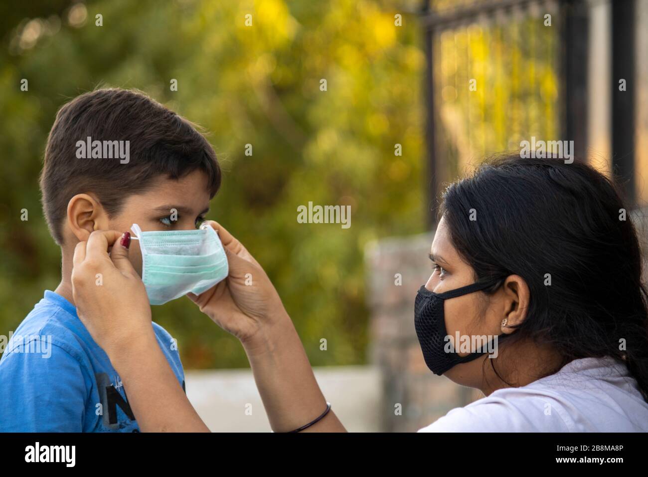 Madre aiutare bambino a indossare maschera in india per proteggerlo contro l'influenza e il virus Foto Stock