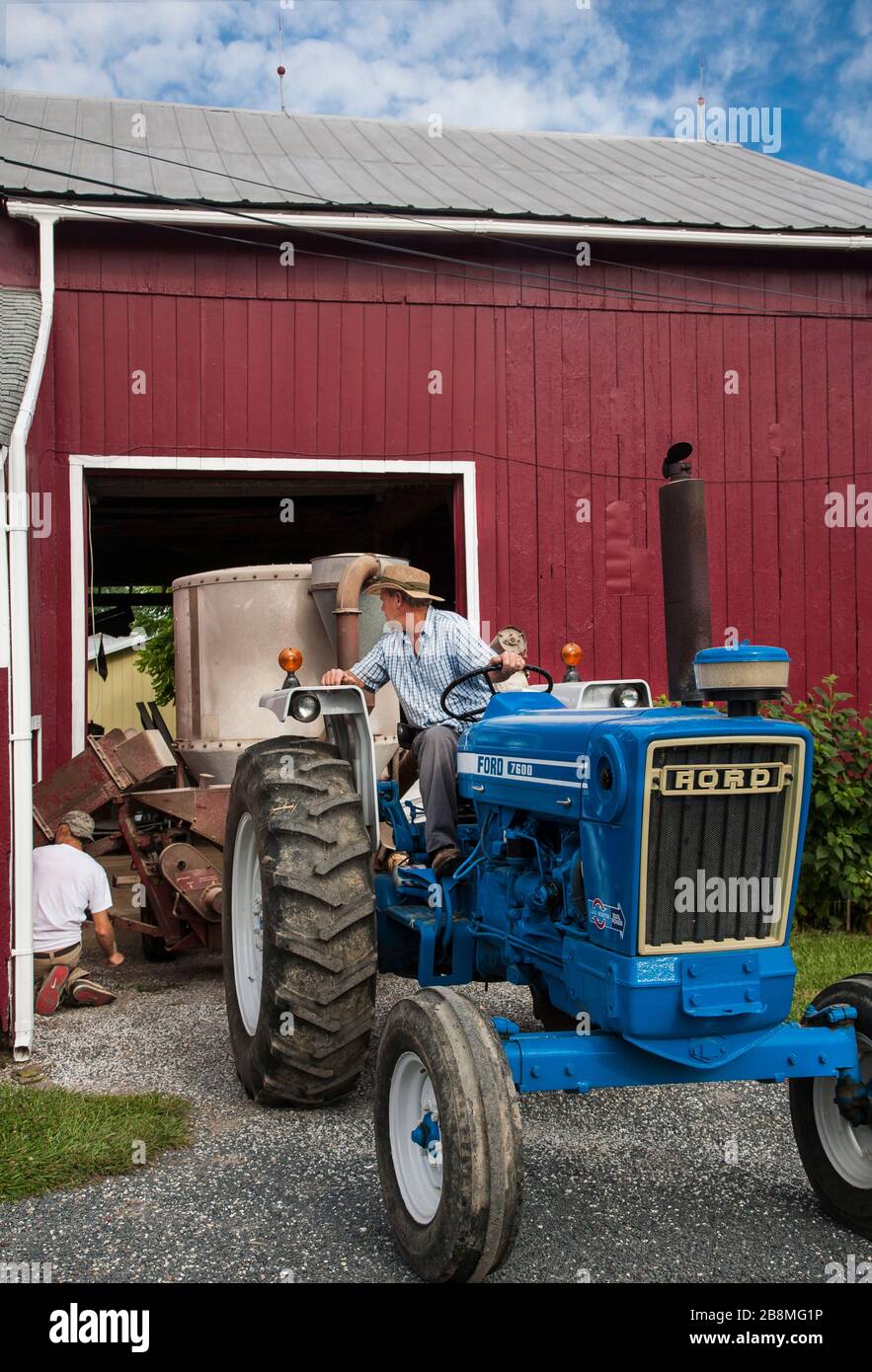 Agricoltore maschio americano su trattore blu, granaio rosso Foto Stock