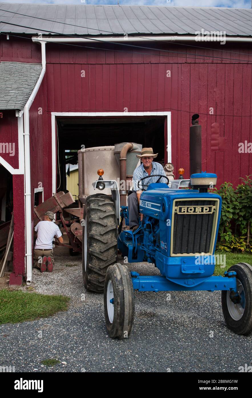 Agricoltore maschio americano su trattore blu, granaio rosso Foto Stock