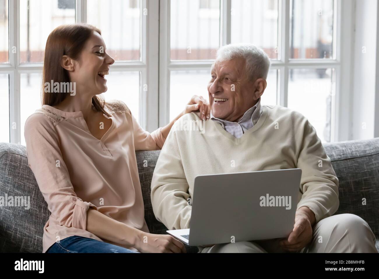 Nipote e nonno adulti che ridono riposandosi con il laptop a casa Foto Stock
