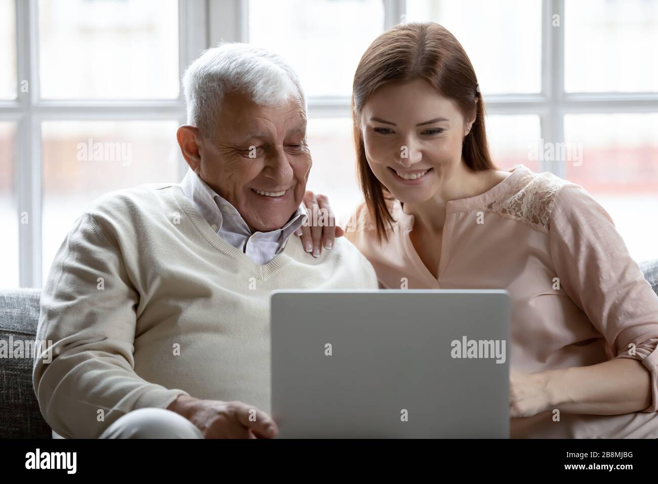 La figlia di Grownup e il padre degli anni '80 si siedono sul divano con il computer portatile Foto Stock