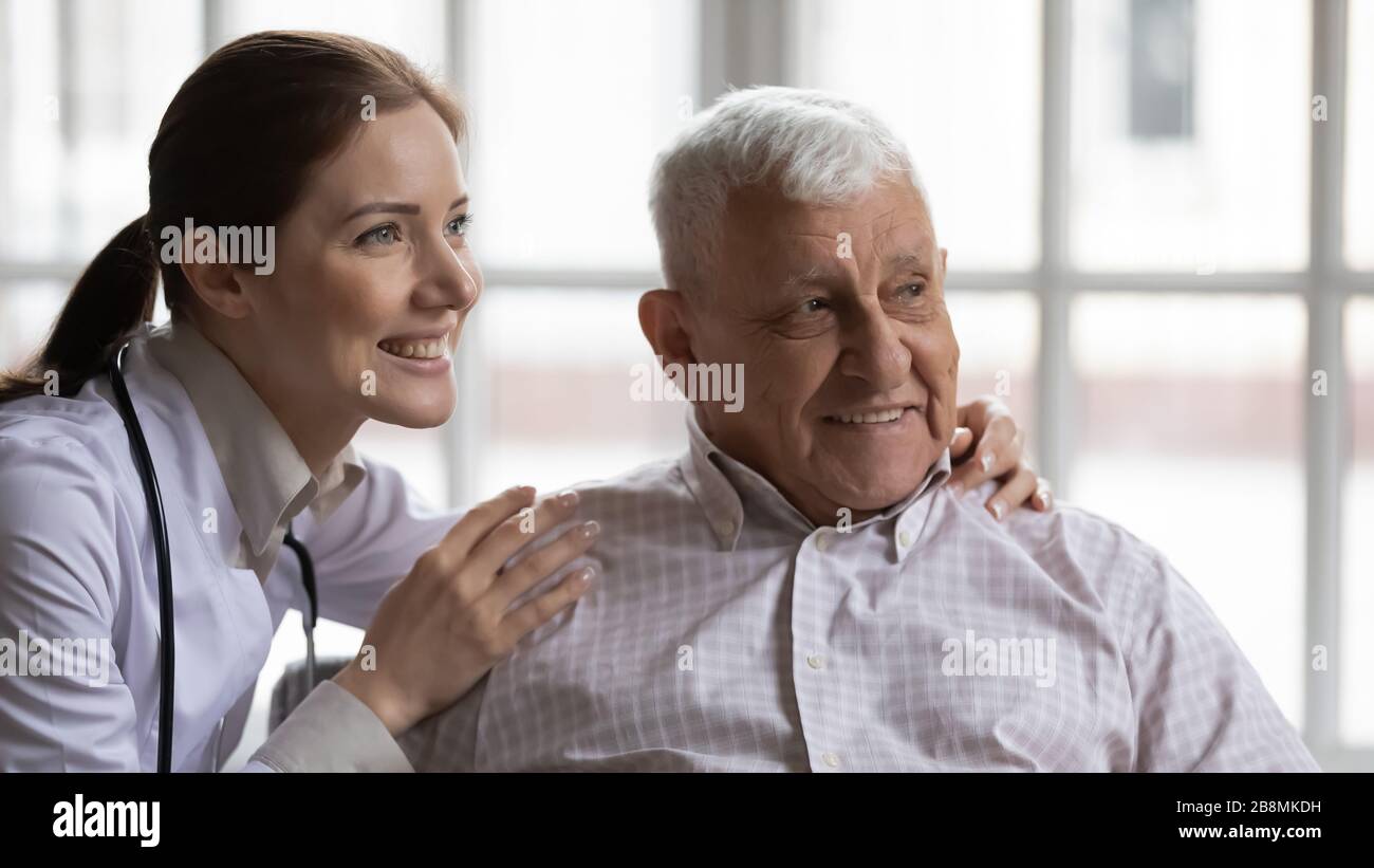 Giovane infermiera abbracca vecchio uomo paziente sorridente guardare a distanza Foto Stock