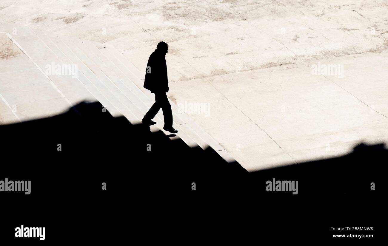 La silhouette ombra di un uomo che cammina da solo giù per le scale della città con vista sepia ad angolo alto Foto Stock