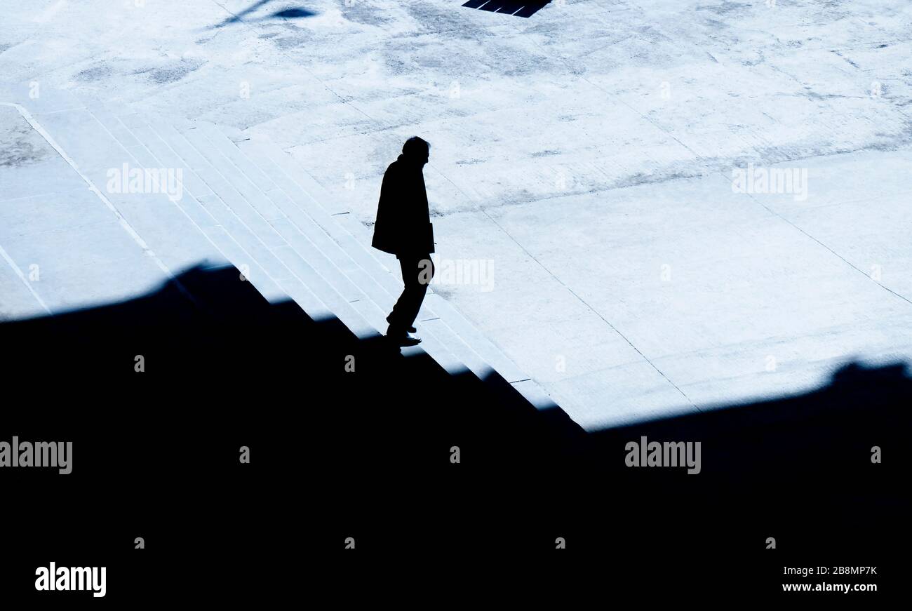 La silhouette ombra di un uomo che cammina da solo giù per le scale della città di notte, vista ad angolo alto Foto Stock