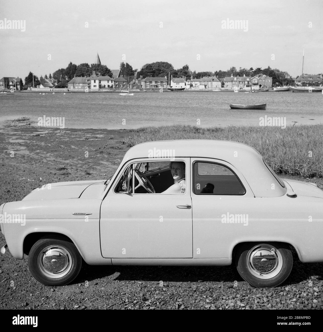 1950, storico, un giorno fuori .... una signora seduta nel sedile del passeggero di una popolare auto dell'epoca, un due porte Ford Anglia 100E, accanto al fiume Frome, vicino Old Sodbury, Inghilterra, Regno Unito. Foto Stock