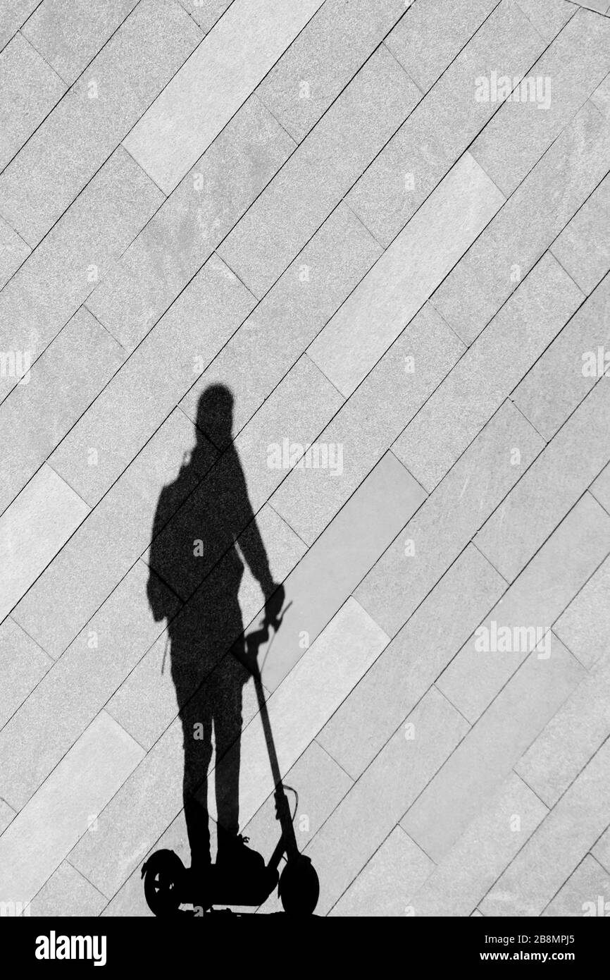 La silhouette ombra di una persona che guida uno scooter elettrico su un marciapiede vuoto della città, in bianco e nero Foto Stock
