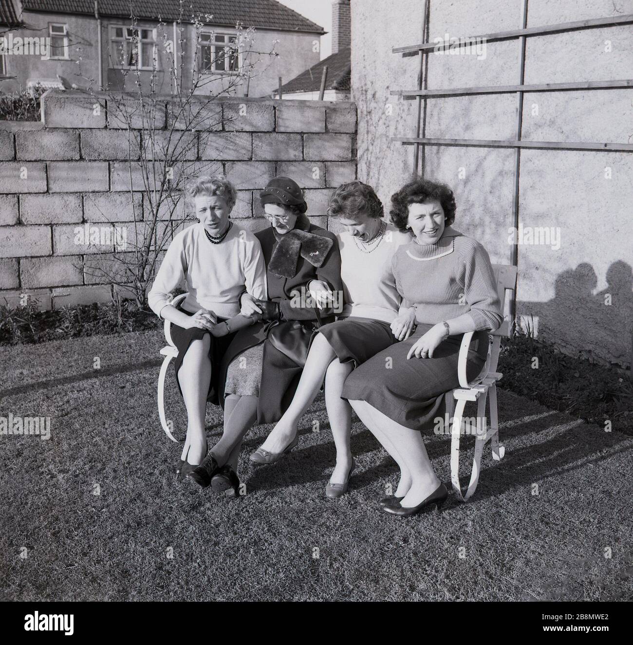 1959, storico, quattro Signore, possibile una madre e le sue tre figlie adulte, seduti a stretto contatto fuori su una panca di metallo in giardino per una foto di famiglia, Inghilterra, Regno Unito. Foto Stock
