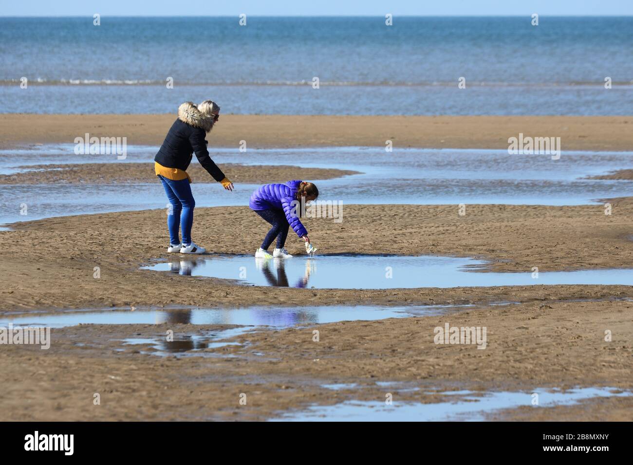 Una madre e una figlia prelevano la lettiera da una piscina su una spiaggia Foto Stock