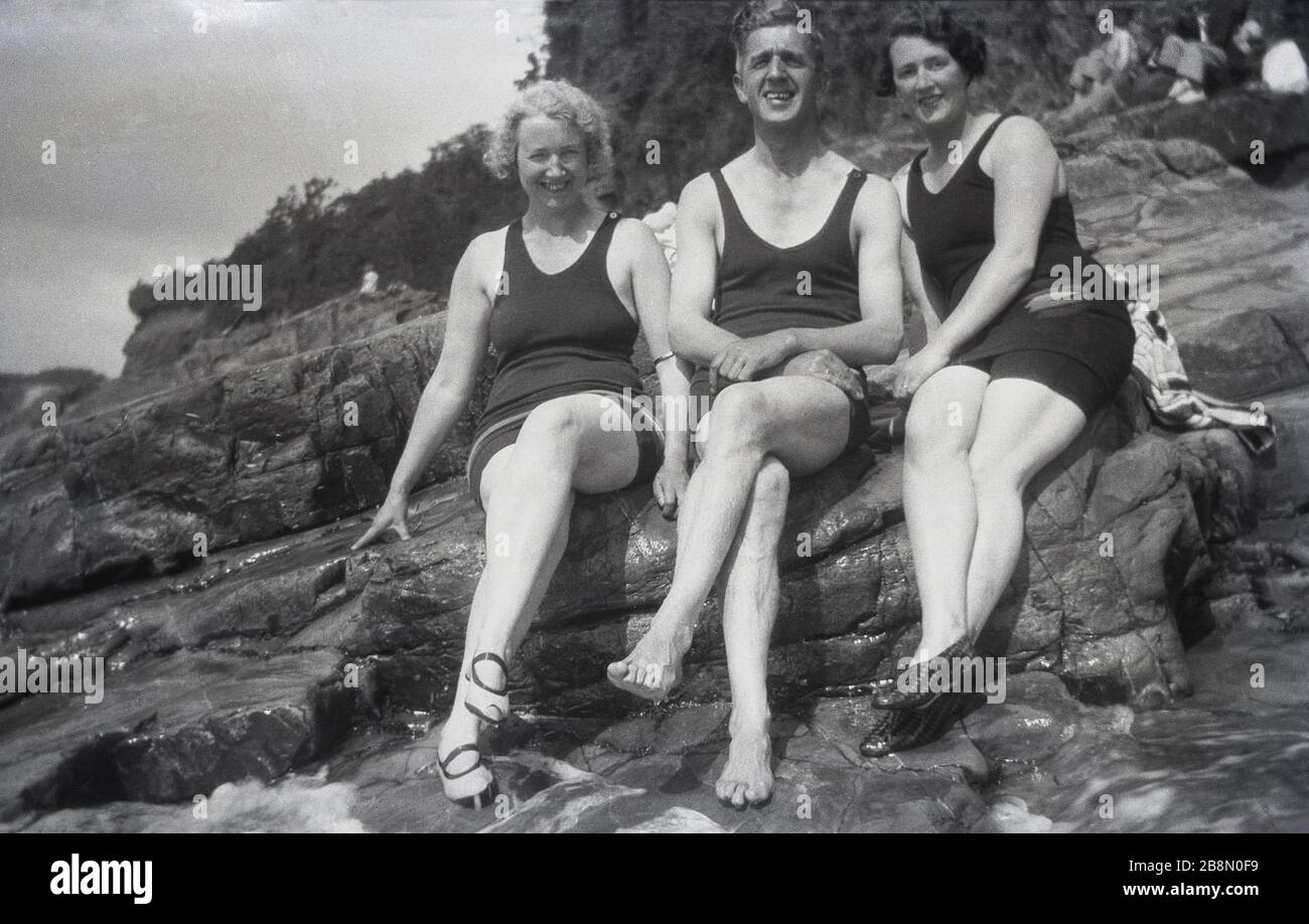 Alla fine degli anni '20, all'inizio degli anni '30, un uomo e due Signore seduti insieme su alcune rocce sulla costa nei costumi da bagno dell'epoca. Foto Stock