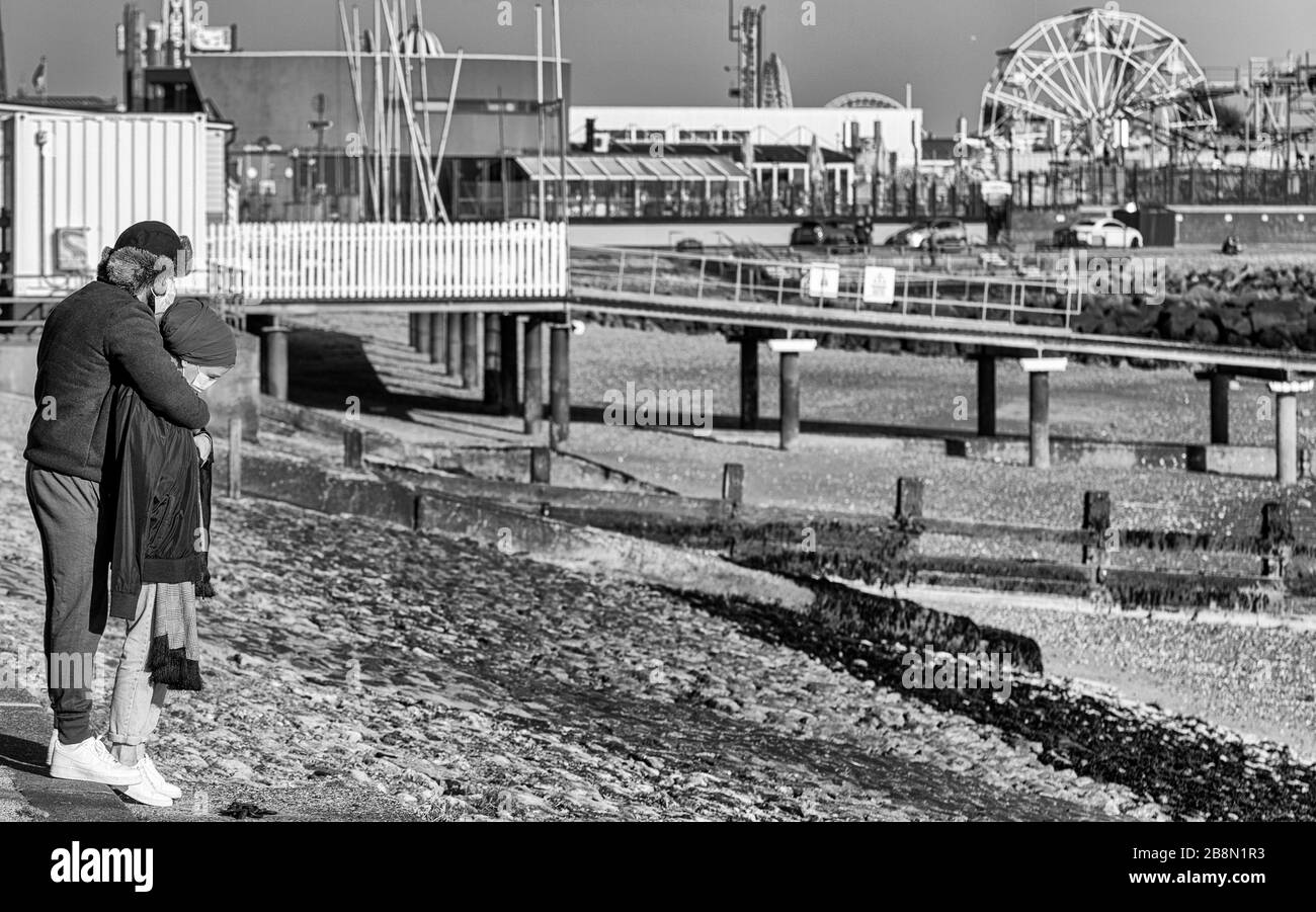 Giovani coppie che indossano maschere facciali sul lungomare di Southend apparentemente preoccupate per il loro futuro a causa della pandemia di COVID-19 Coronavirus. Monocromatico Foto Stock