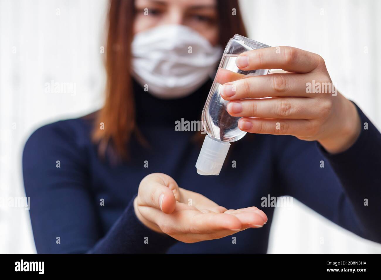Donna in maschera medica protettiva applicazione di un gel antisettico per la disinfezione delle mani e la protezione contro il virus influenzale. Quarantena del coronavirus. Foto Stock