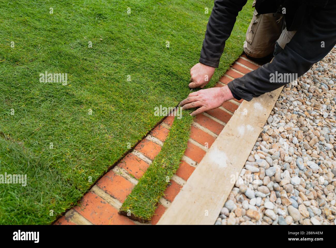 Un uomo che rifinisca il nuovo tappeto erboso naturale lungo la striscia di tosatura in mattoni ai margini del prato Foto Stock