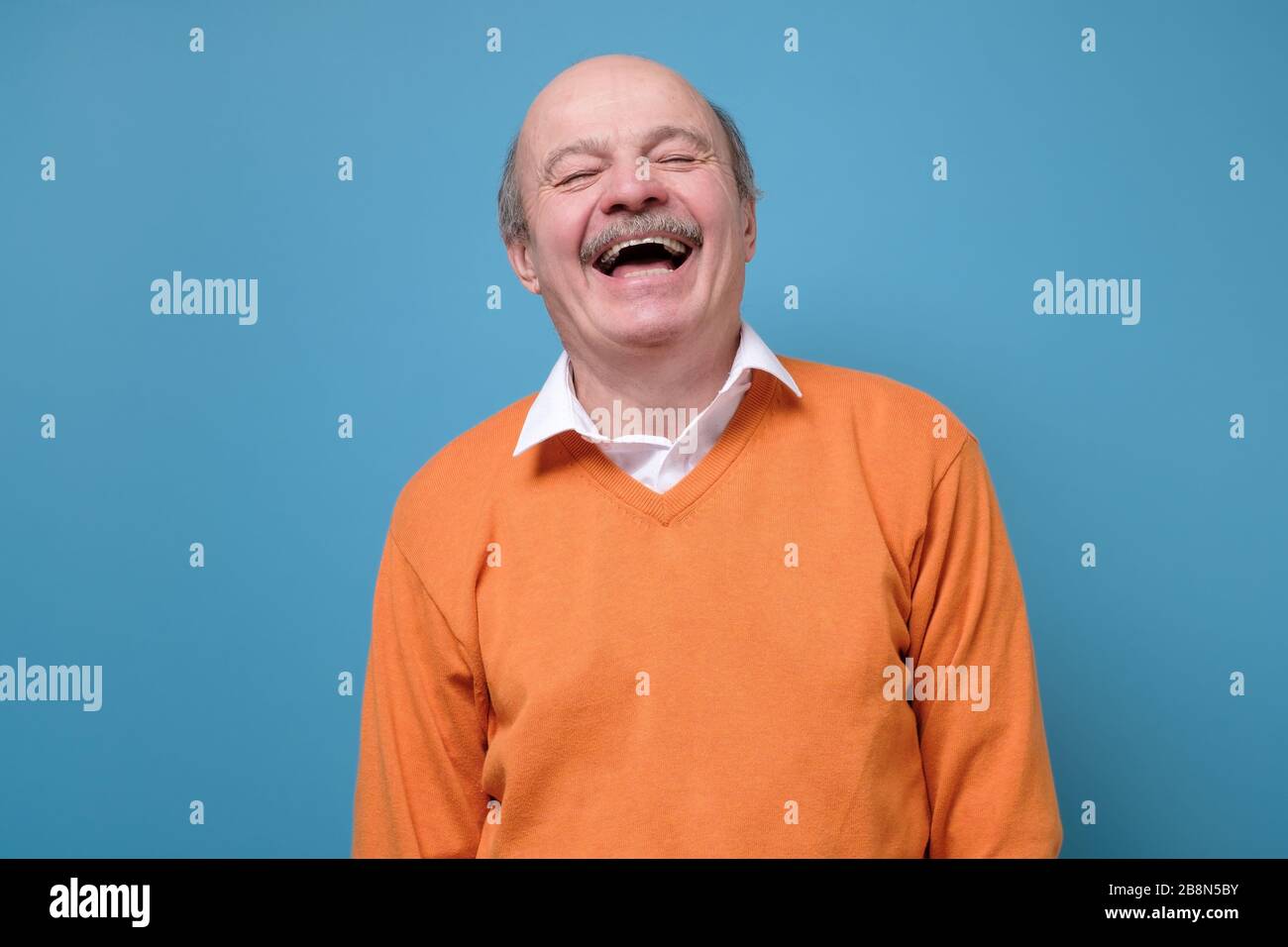 Uomo ispanico anziano in maglia arancione ridendo in scherzo. Foto Stock