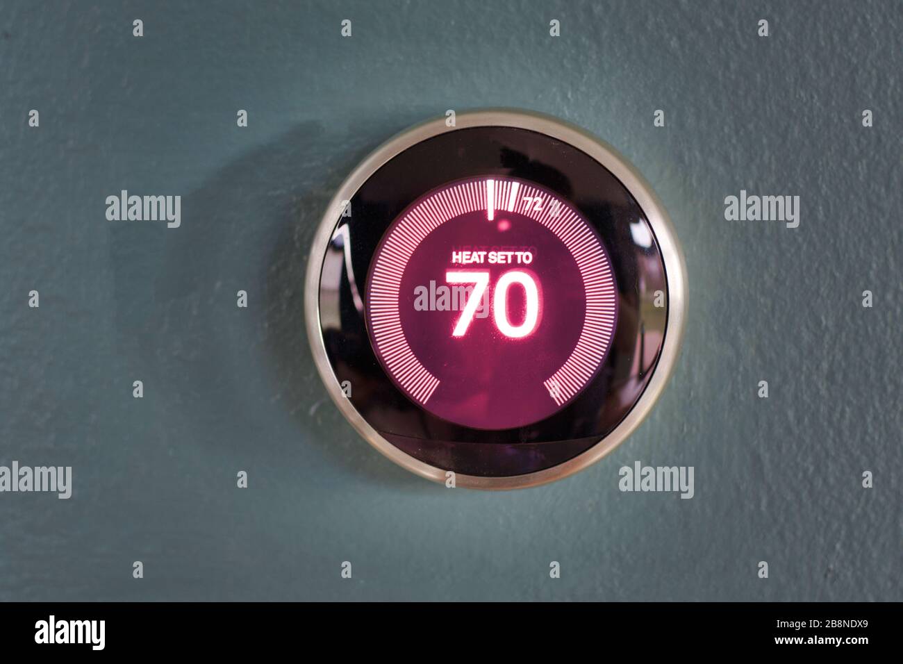 Termostato domestico intelligente NEST con informazioni centrali rosse sulla parete blu. Riscaldamento della temperatura di casa a 70 gradi. Foto Stock