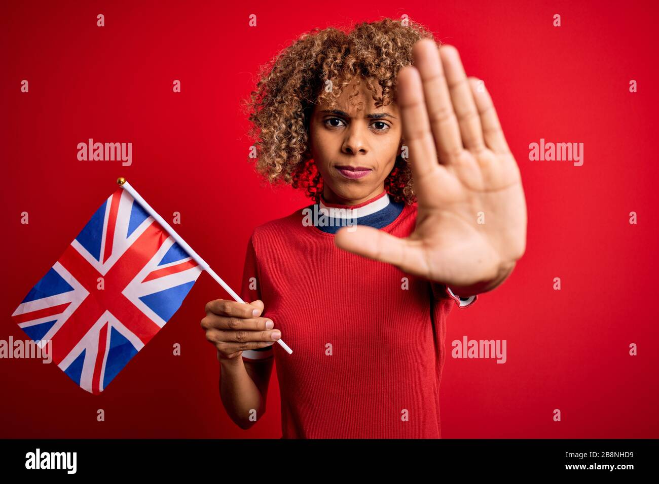 Giovane maledetta afro-americana che tiene la bandiera del regno unito per celebrare il referendum sulla brexit con la mano aperta facendo stop sign con espressione seria e fiduciosa, Foto Stock