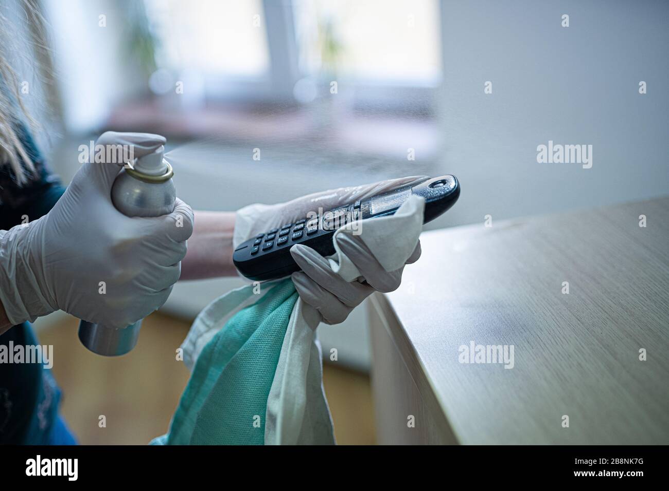 Donna disinfetta il telefono con un liquido disinfettante spray. Foto Stock