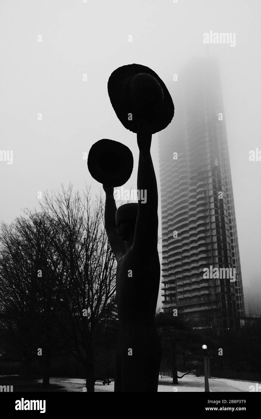 Colpo bianco e nero dell'uomo con due gatti (da Henk Visch) che tiene in su i suoi cappelli davanti ad una nebbia protetto condominio a Ottawa, Ontario, Canada. Foto Stock