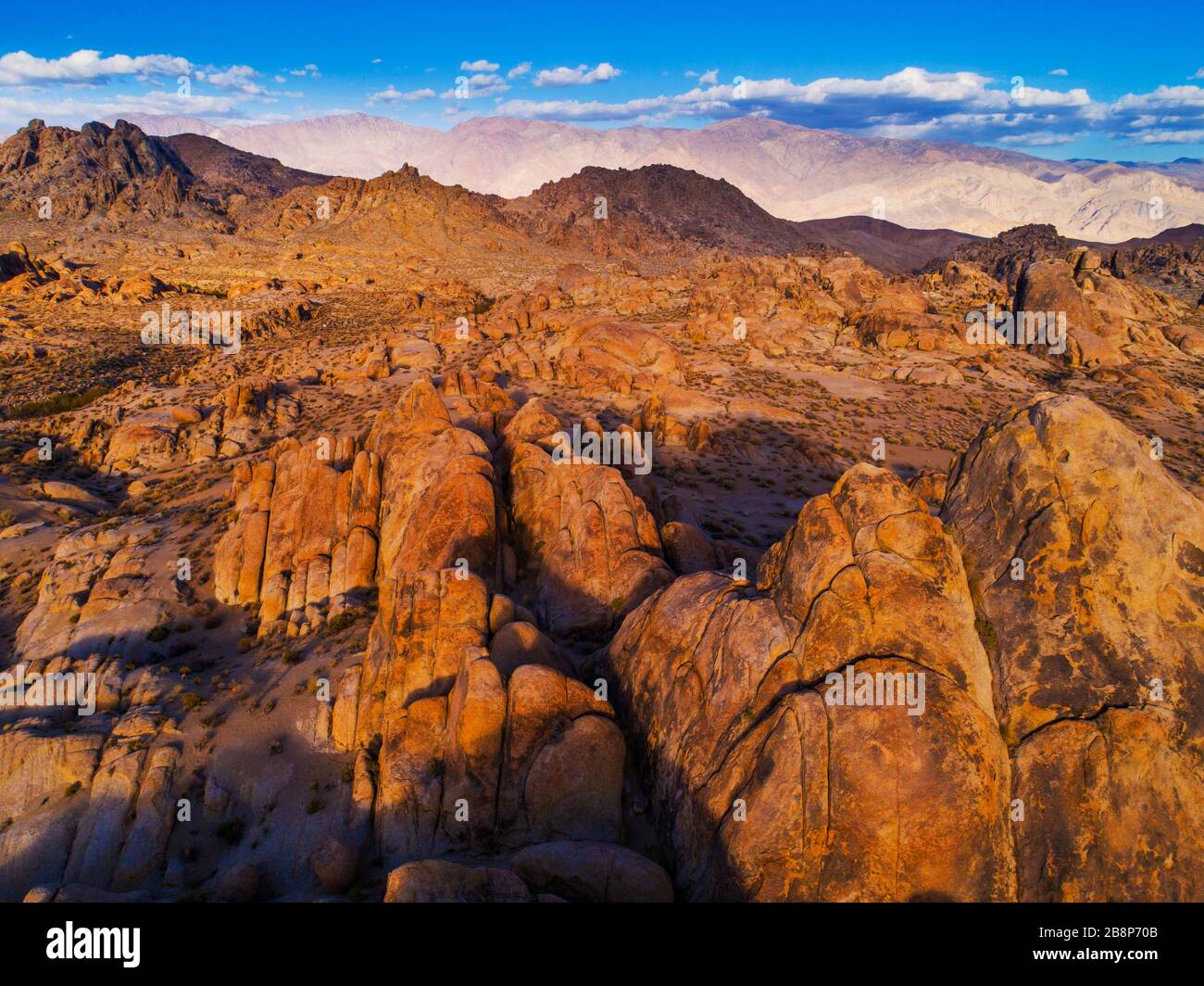 Vista aerea delle formazioni rocciose delle colline dell'Alabama con i Monti Inyo in lontananza al tramonto. Foto Stock