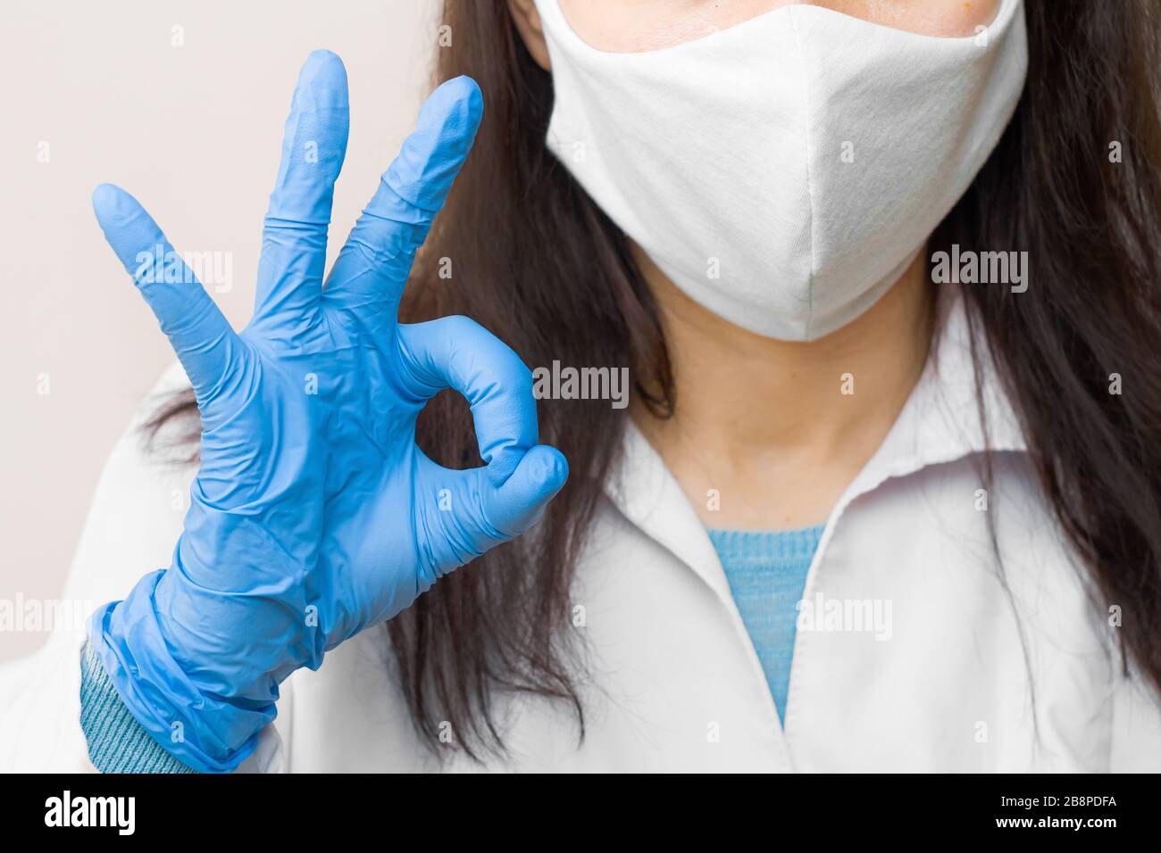 Donna mostra ok in guanti blu e maschera protettiva nella lotta con coronavirus, 2019-nCoV, SARS-Cov-2, influenza. Concetto di assistenza sanitaria e buona medicina. Foto Stock