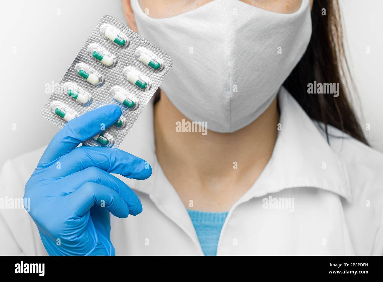 Prevenzione del coronavirus assunzione di vitamine per rafforzare l'immunità. Medico in maschera protettiva e guanti blu con pillole nelle mani. Foto Stock