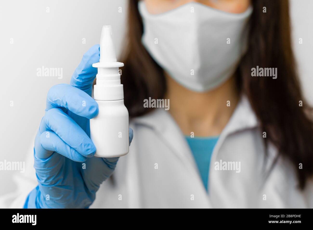 Una donna che usa spray nasale per il trattamento dell'influenza o il naso che corre tiene il medicinale in mano. Il medico in maschera protettiva e guanti blu mostra spray nasale per Foto Stock