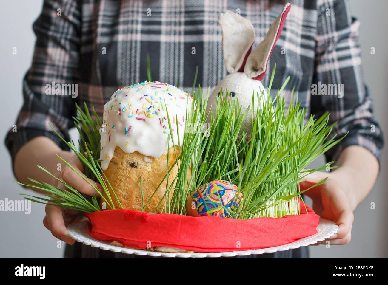 Tradizionale torta di Pasqua, uova e coniglietto in erba in mani femminili. Pane di Pasqua con crema bianca e decorazione colorata sulla parte superiore. Festa Foto Stock