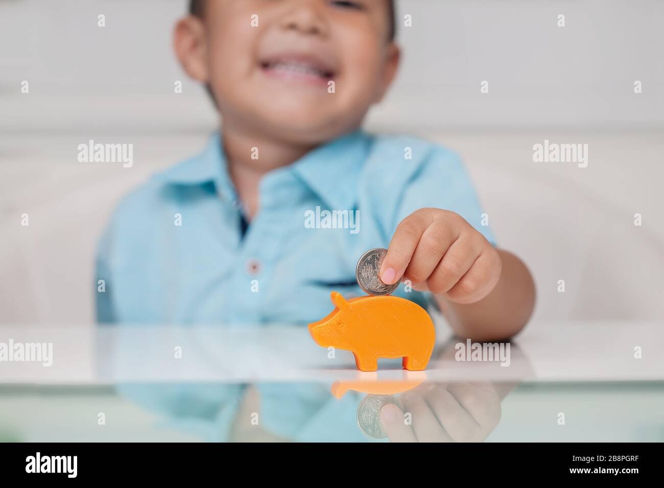 ragazzo di 4 anni che mette una moneta in una piccola banca del piggy, usando una presa inferiore della pinza e mostrando la fiducia. Foto Stock