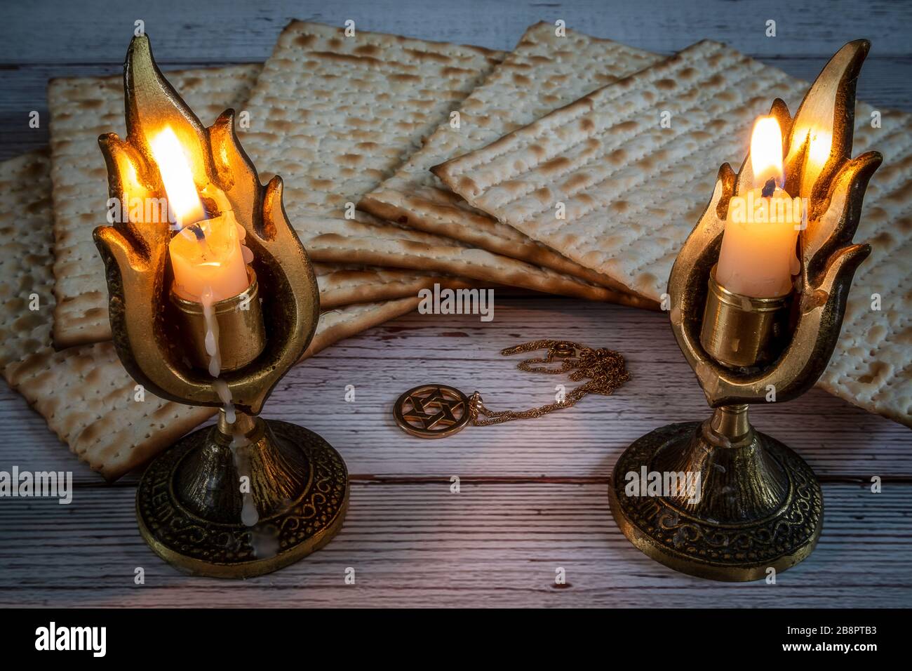 Pasover matzos, due candelabri con candele bruciate, e stella della collana David su sfondo di legno Foto Stock