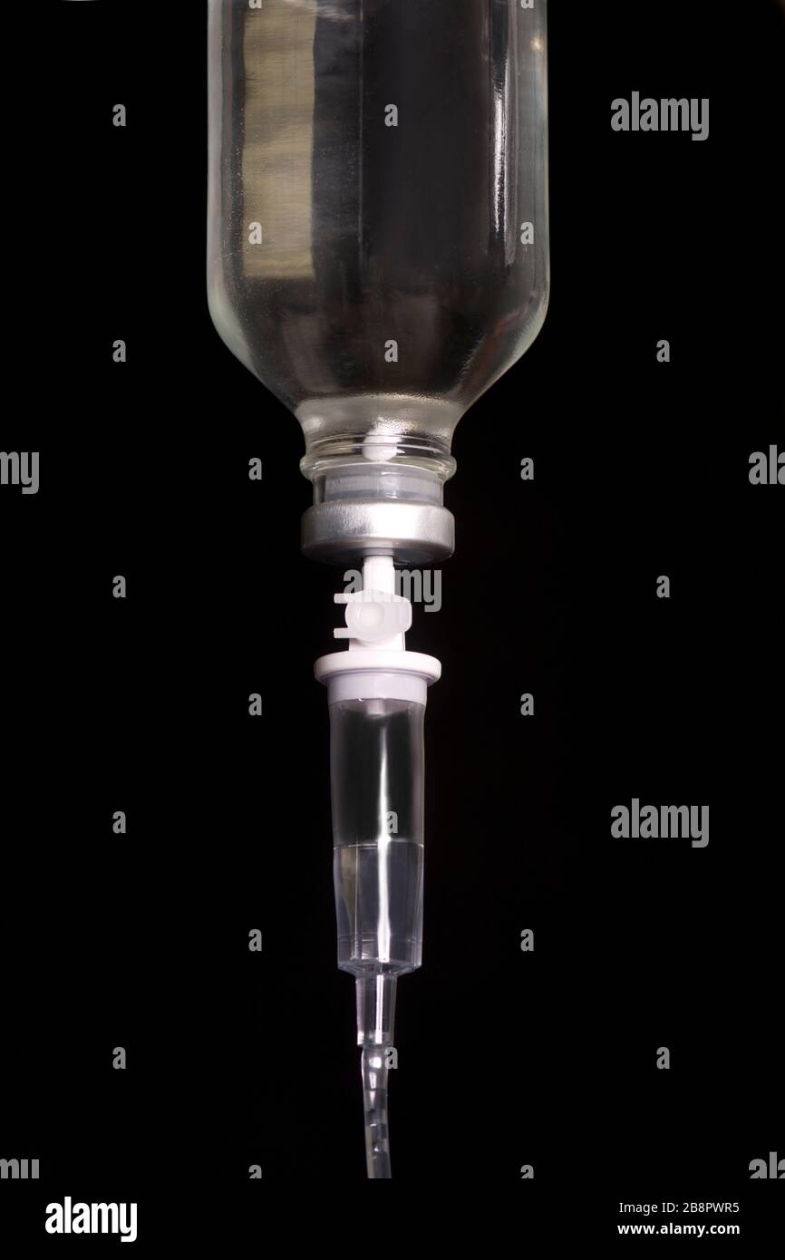 Flacone IV in vetro con camera di gocciolamento IV e tubo IV su sfondo scuro. Foto Stock