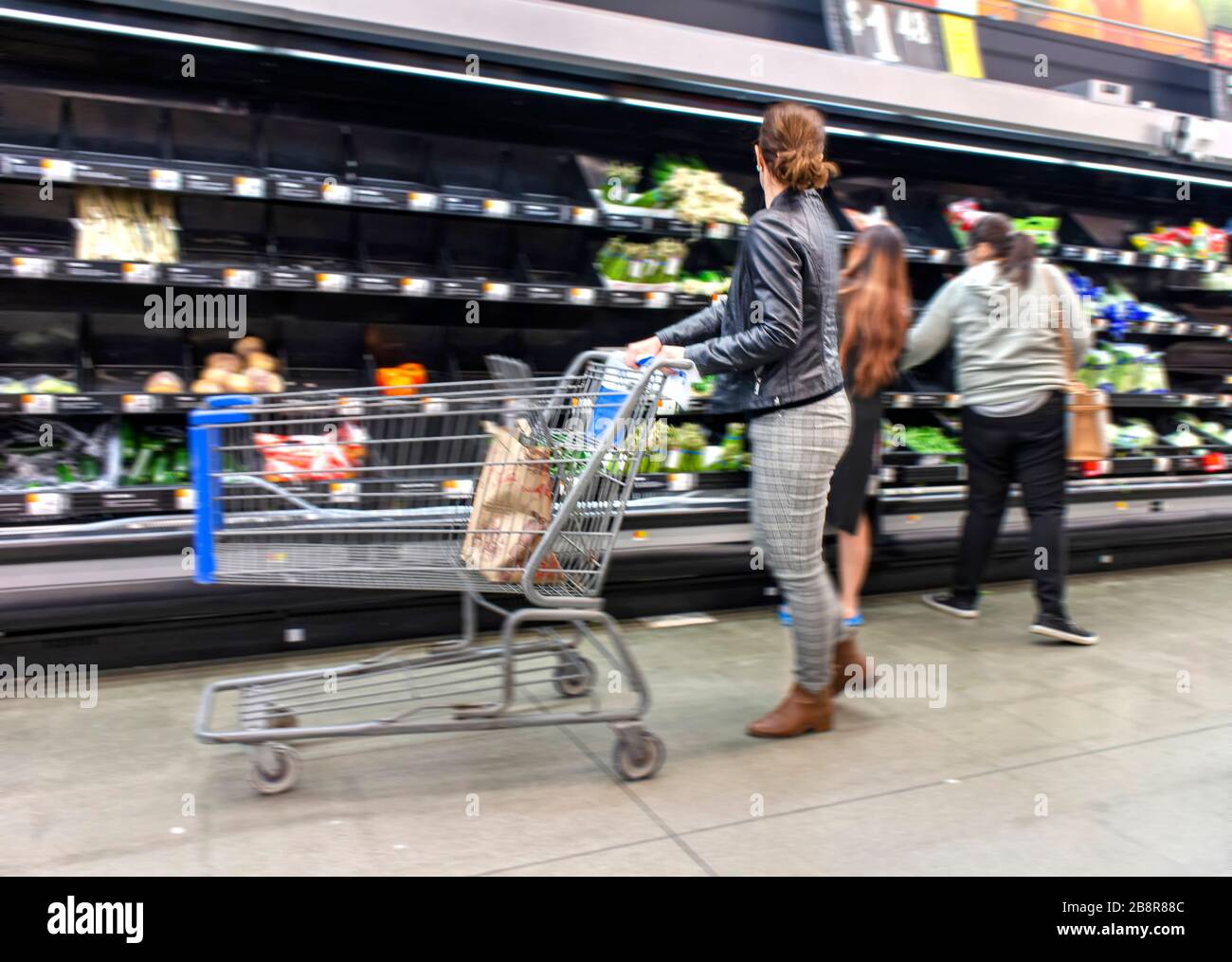 Persone che acquistano tra scaffali vuoti in un supermercato durante la pandemia coronavirus Foto Stock