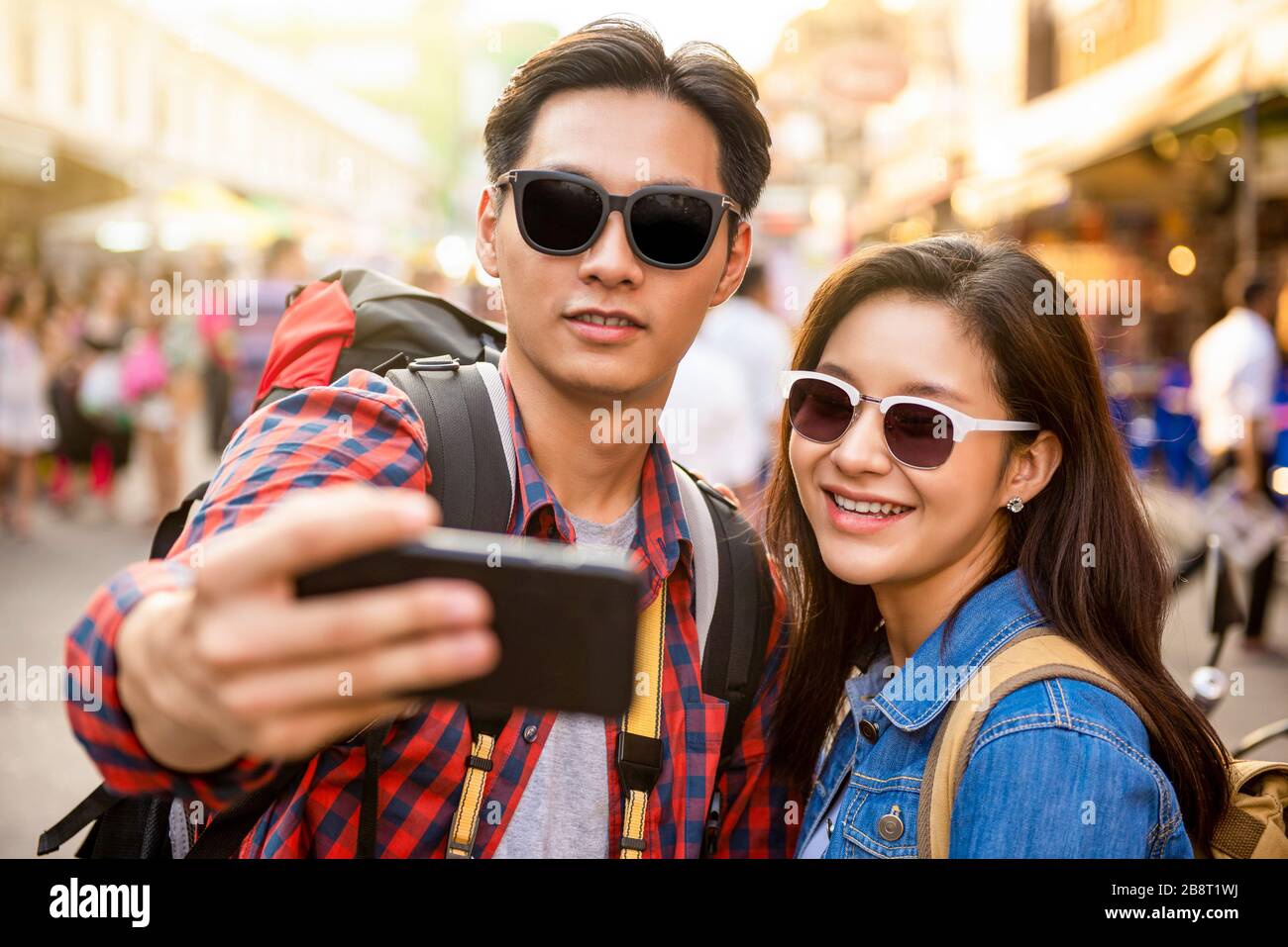 Sorridente giovane coppia asiatica turisti che prendono selfie mentre viaggiano in Khao San Road Bangkok Thailandia durante le vacanze estive Foto Stock