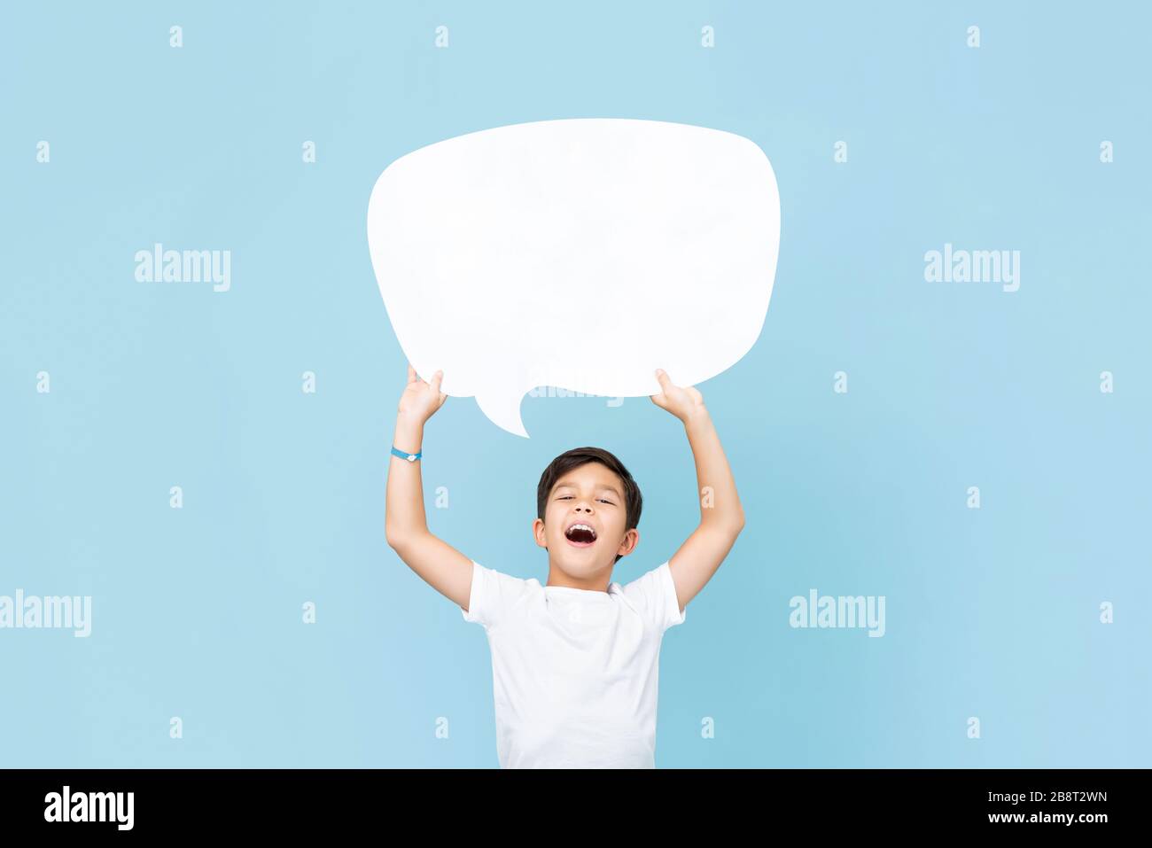 Girovita su ritratto di ragazzo asiatico sorridente che tiene in su una bolla bianca vuota del discorso in uno sfondo blu chiaro dello studio Foto Stock