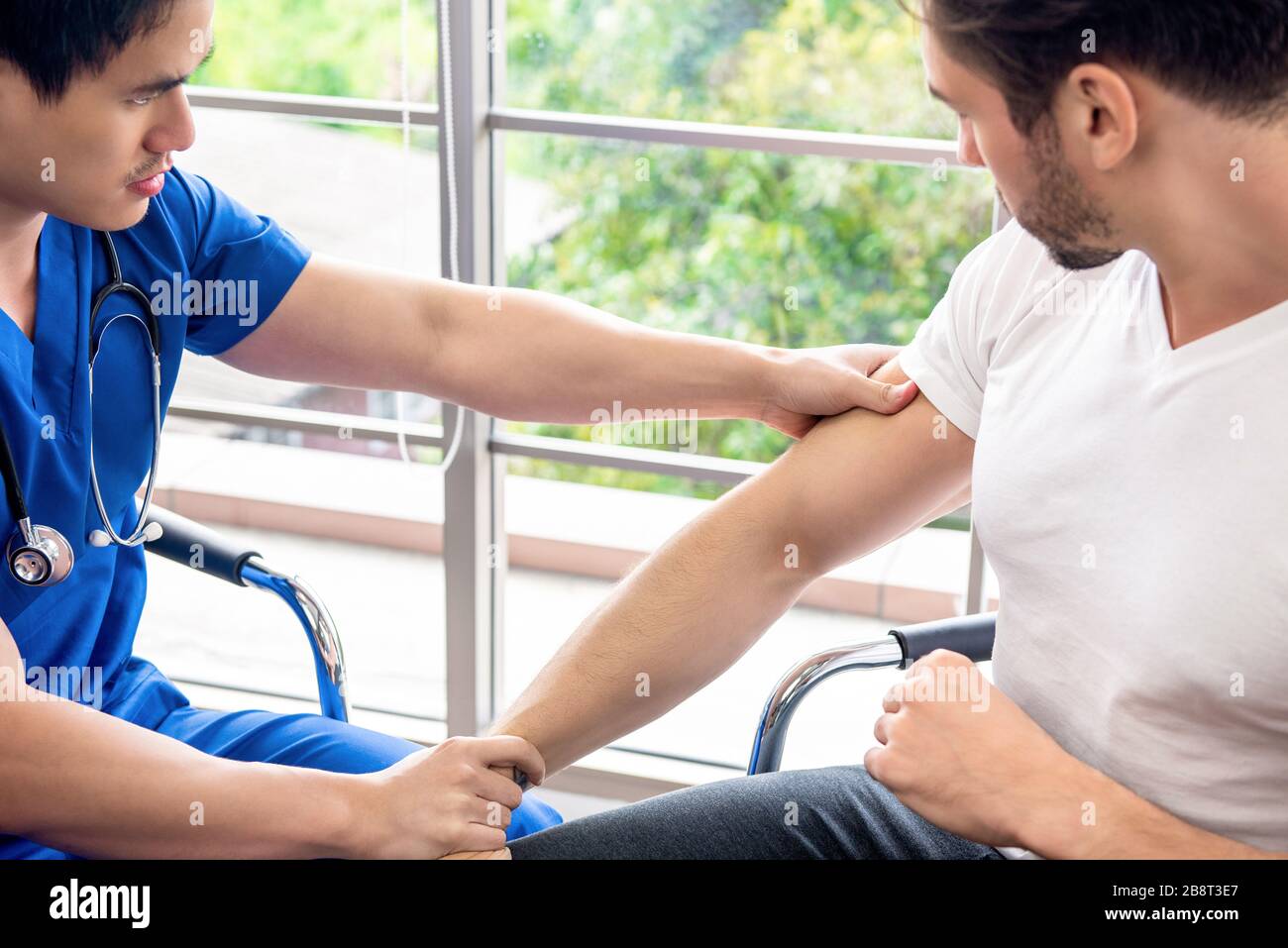 Medico asiatico braccio massaggiante di atleta paziente maschile in clinica per il concetto di terapia fisica Foto Stock