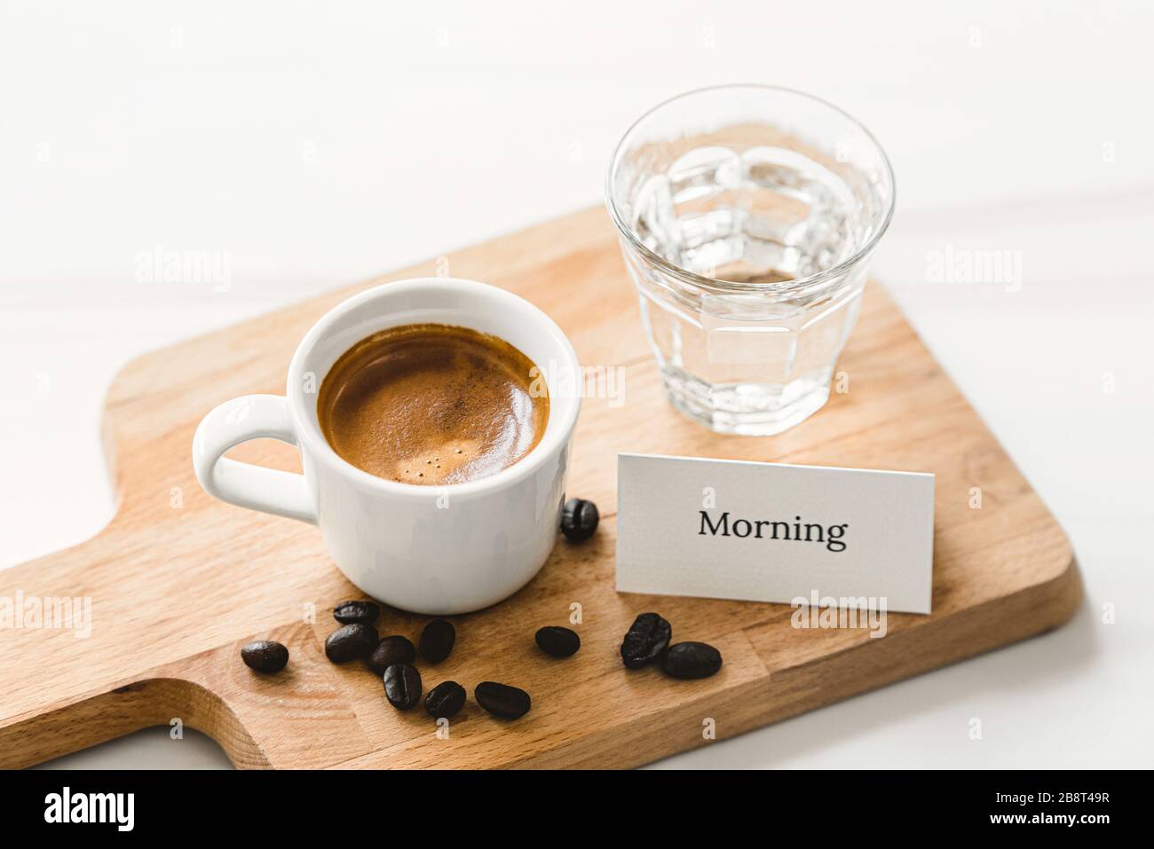 Una tazza di caffè espresso appena preparato viene servita per colazione su un piatto di legno con un biglietto di auguri per la buona mattina Foto Stock