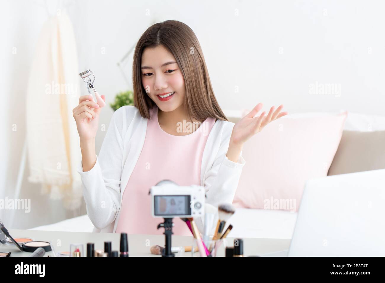 Giovane donna asiatica attraente vlogger di bellezza che tiene arricciacapelli eyelash facendo streaming live di fronte alla fotocamera Foto Stock