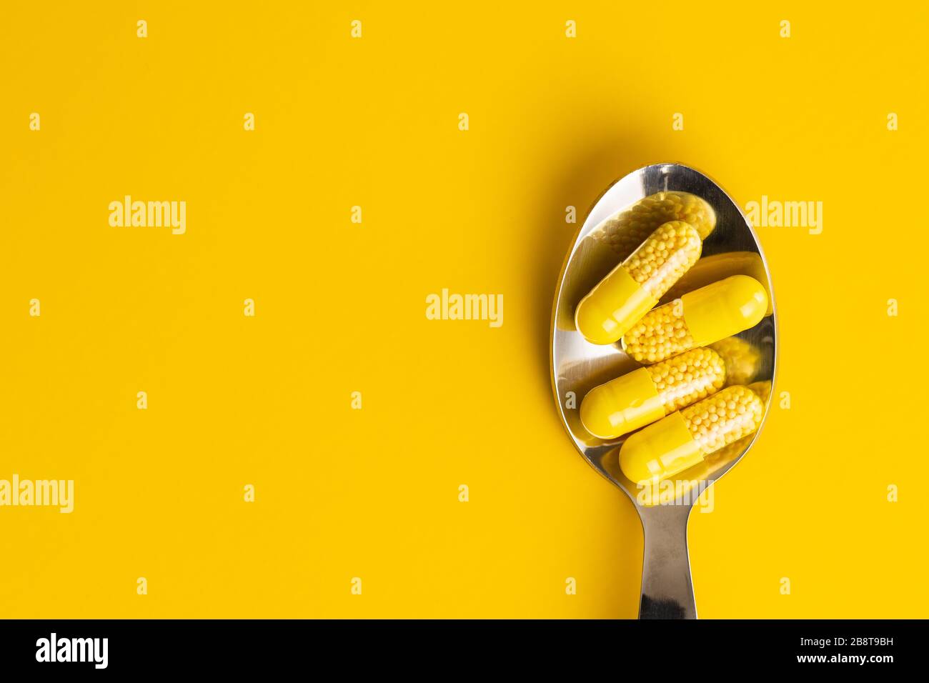Capsule vitaminiche. Pillole di vitamina C in cucchiaio su sfondo giallo. Vista dall'alto. Foto Stock