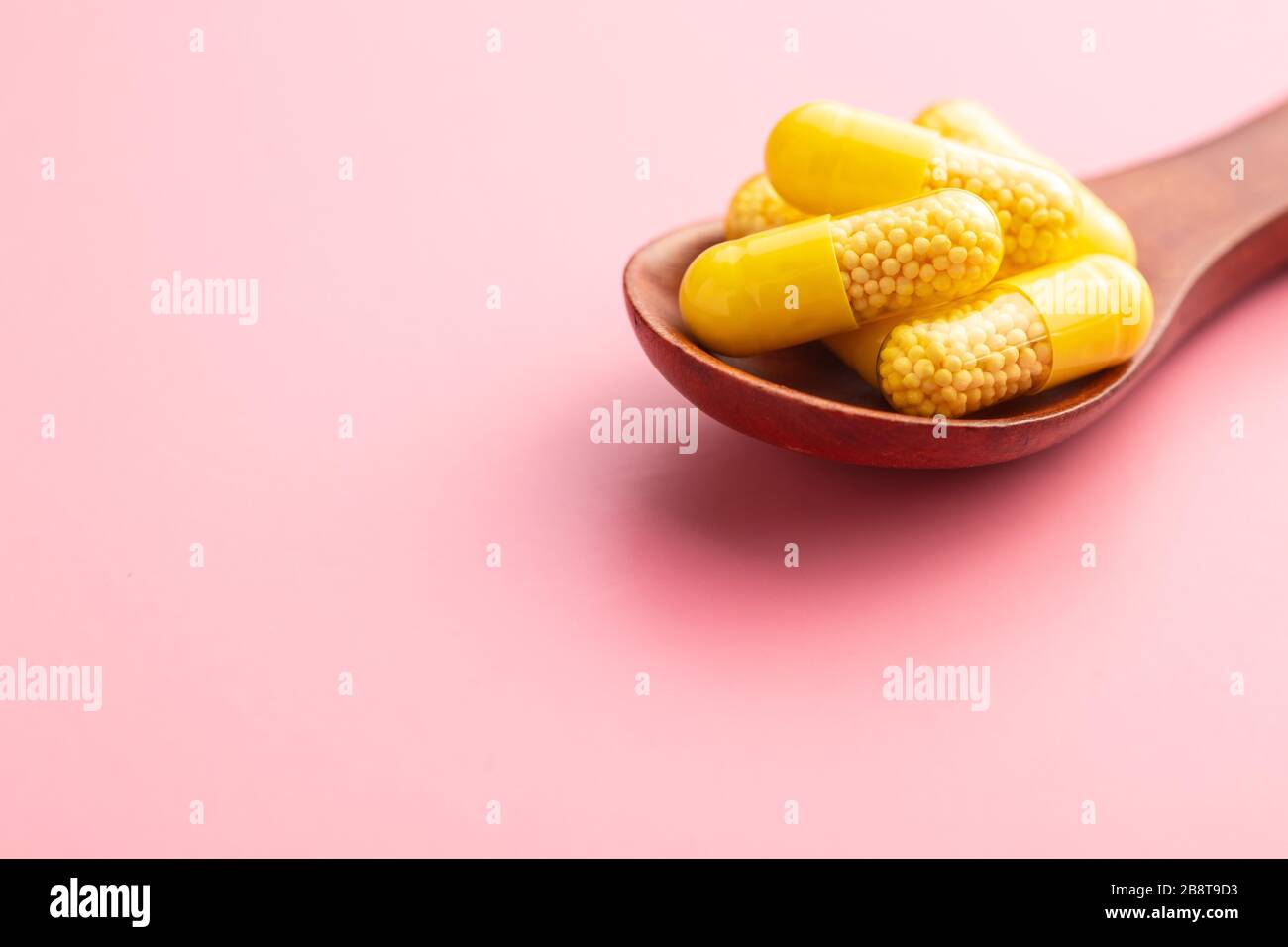 Capsule vitaminiche. Pillole di vitamina C in cucchiaio di legno su sfondo rosa. Foto Stock