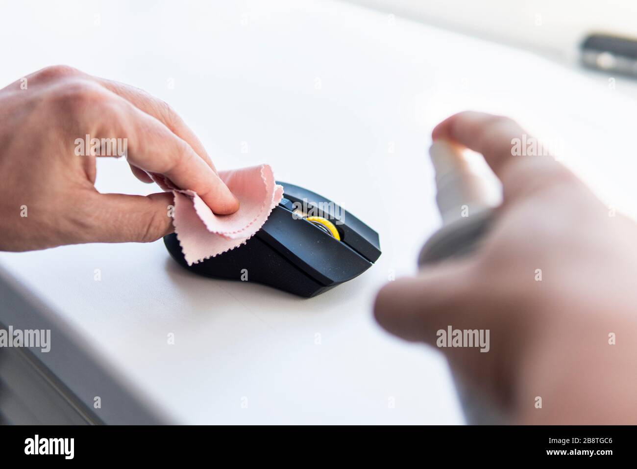 Un uomo strofina un topo sporco con uno straccio . Pulizia del mouse del computer. Rimozione dei microbi con una soluzione alcolica o antisettica. Prevenzione di coronaviru Foto Stock