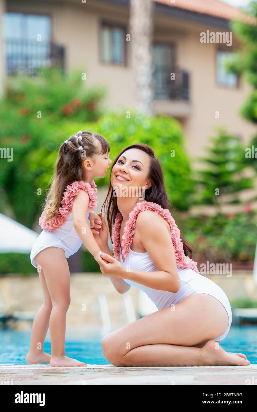 Mamma giovane con bambina negli stessi costumi da bagno bianchi seduti sul  bordo della piscina. Amore e bacio. Abbigliamento per estate e mare in  famiglia look Foto stock - Alamy