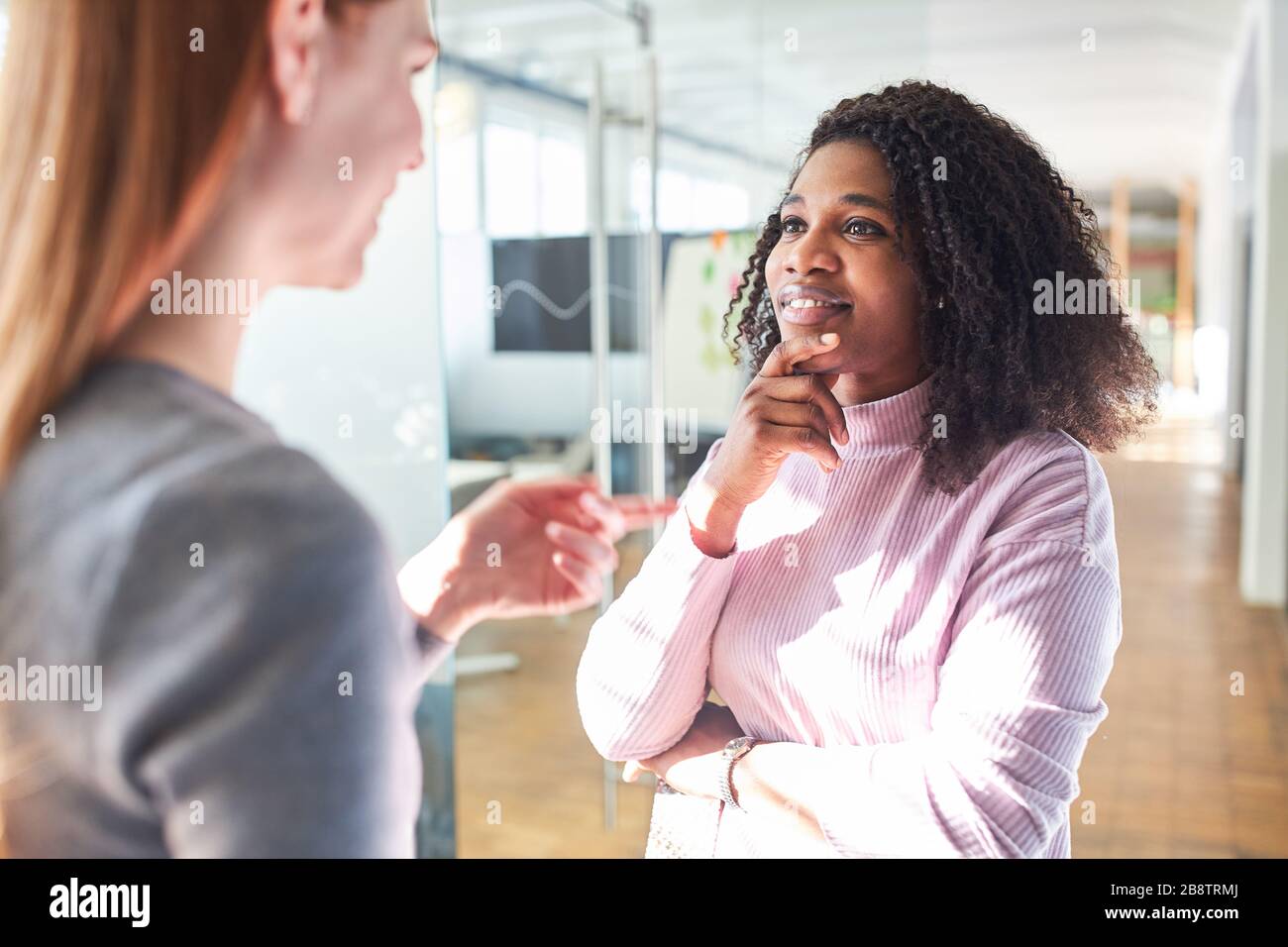 Donna africana in dialogo o piccolo parlare con un collega in ufficio Foto Stock