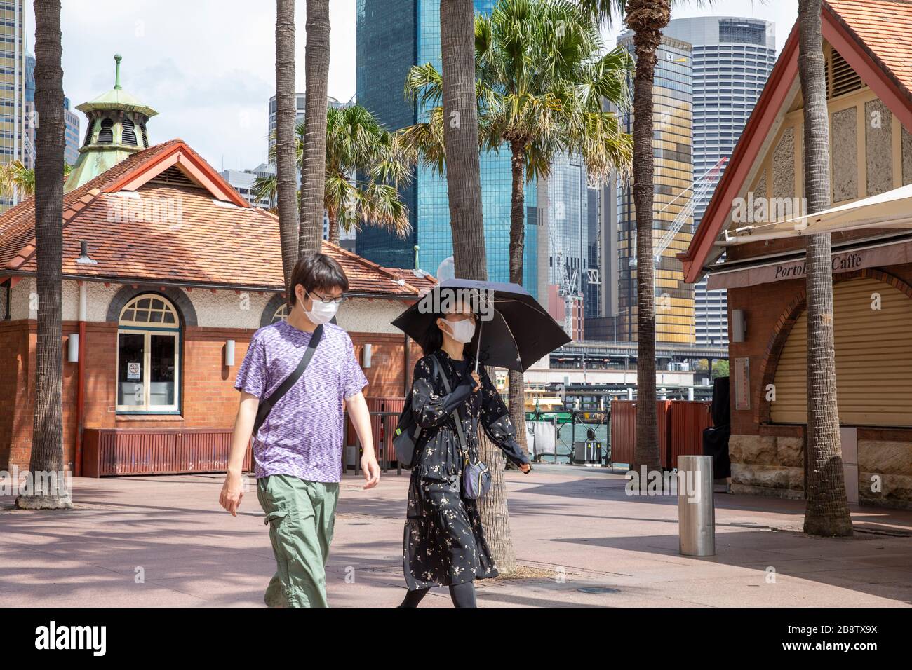Centro di Sydney, Australia. Lunedì 23 Marzo 2020. Le coppie asiatiche indossano maschere facciali mentre camminano accanto a caffè chiusi a Circular Quay. Credit Martin Berry/Alamy Live News Foto Stock