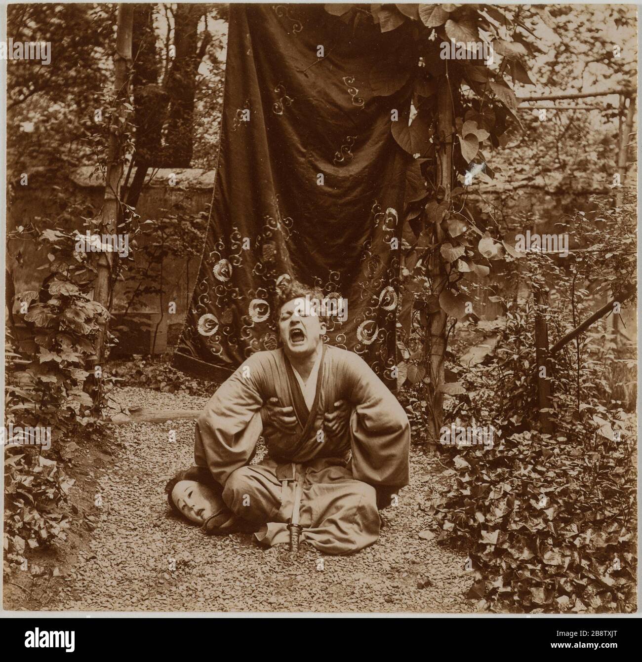 Comico seduto a gambe incrociate in un giardino con un abito tradizionale giapponese che gridava, la testa della donna in una delle sue ginocchia. Acteur assis en tailleur dans un jardin vêtu d'un costume tradizionnel japonais en train de crier, tête de femme sous l'un de ses genoux. Anonima fotografa, vers 1900. Parigi, musée Carnavalet. Foto Stock