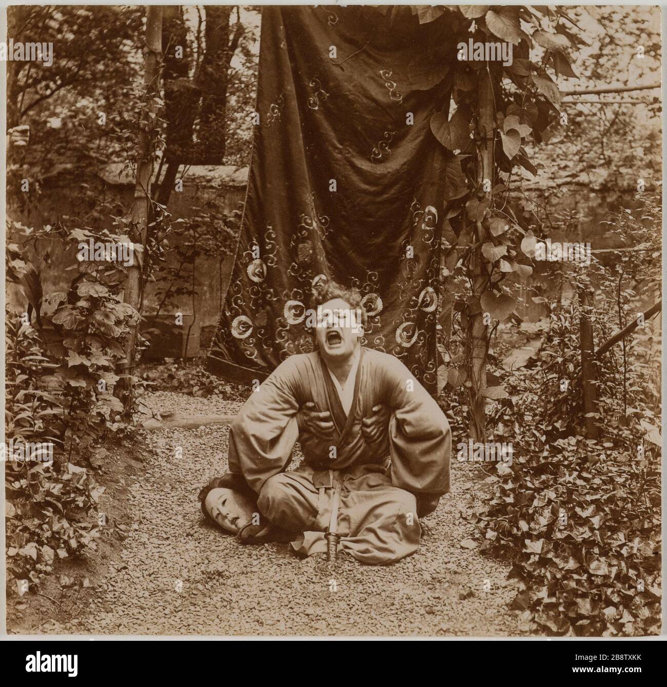 Comico seduto a gambe incrociate in un giardino con un abito tradizionale giapponese che gridava, la testa della donna in una delle sue ginocchia. Acteur assis en tailleur dans un jardin vêtu d'un costume tradizionnel japonais en train de crier, tête de femme sous l'un de ses genoux. Anonima fotografa, vers 1900. Parigi, musée Carnavalet. Foto Stock