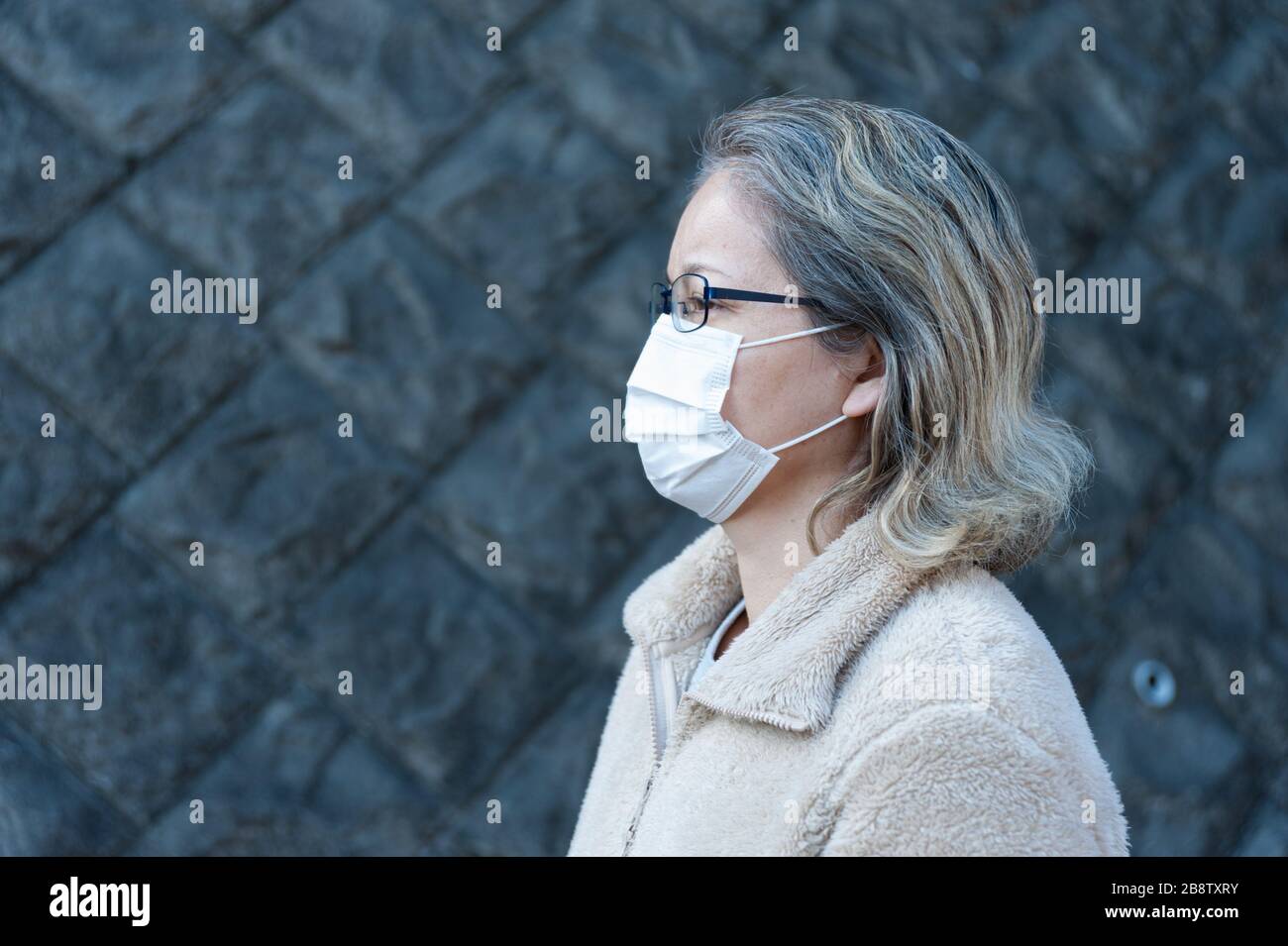 Donna 40-49 anni all'aperto con occhiali e maschera bianca per proteggere contro virus, influenza, febbre da fieno e altre malattie. Guardando al lato. Foto Stock