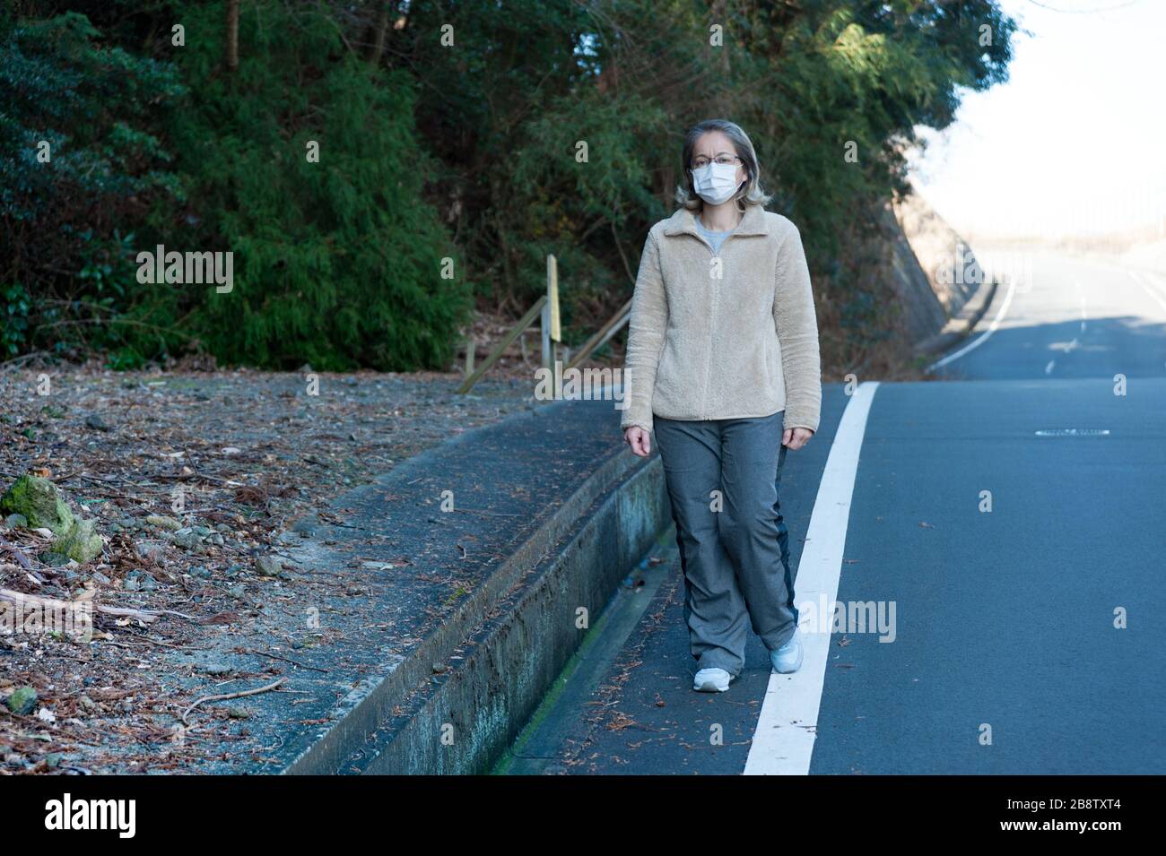 Donna 40-49 anni all'aperto con occhiali e maschera bianca per proteggere contro virus, influenza, febbre da fieno e altre malattie. Camminando sulla strada. Foto Stock
