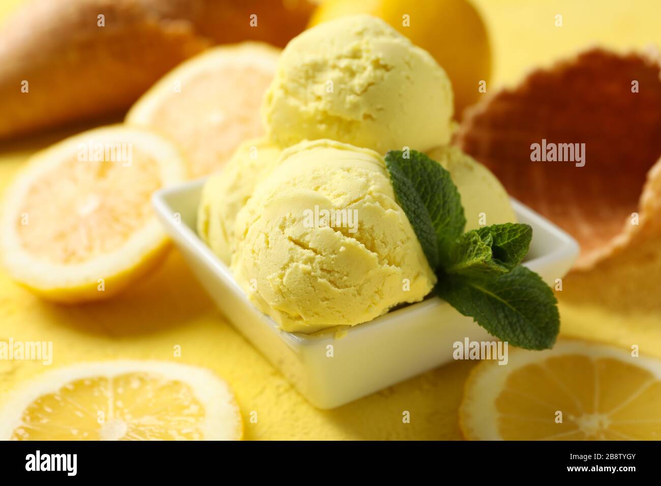 Gelato, cucchiaio, limone e waffle su sfondo giallo, primo piano Foto Stock