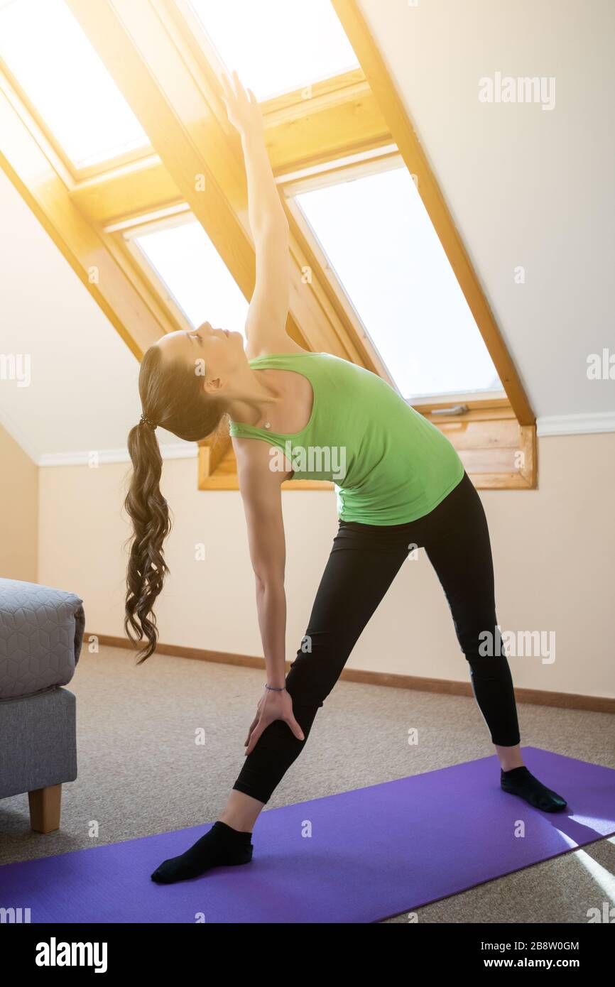 La giovane donna pratica lo yoga a casa. Trikonasana / Bikram triangolo a destra Foto Stock