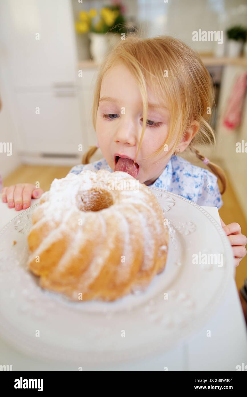 Il bambino lecca segretamente lo zucchero dalla torta fresca in cucina Foto Stock