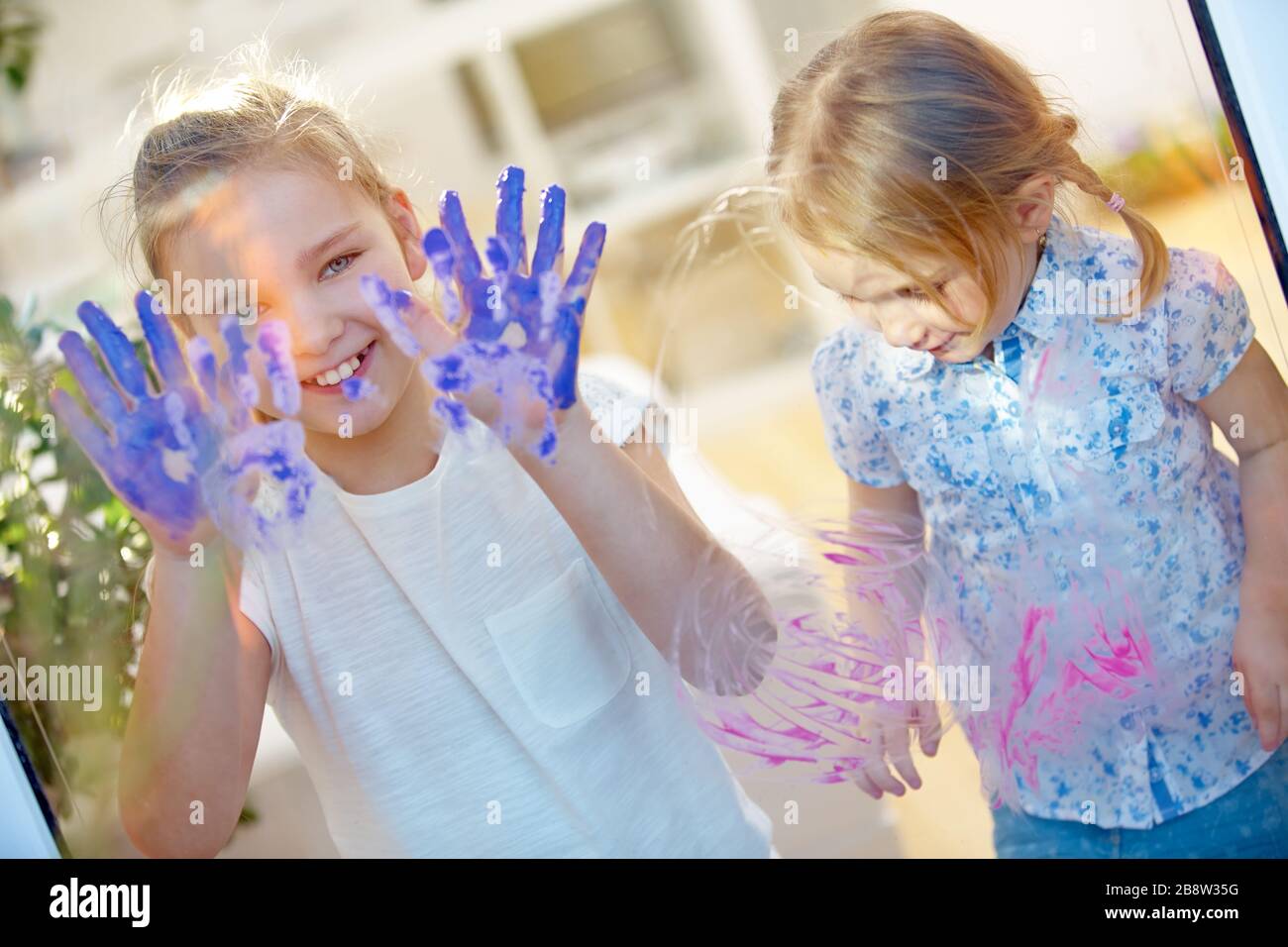 I bambini disegnano le impronte digitali su un vetro con le loro pitture per le dita e le mani Foto Stock